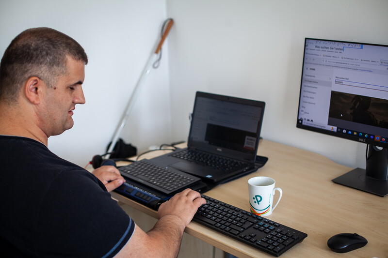 Inklusive Teams: Blindes Teammitglied sitzt am Arbeitsplatz und bedient mit zwei Tatstaturen seinen Rechner.